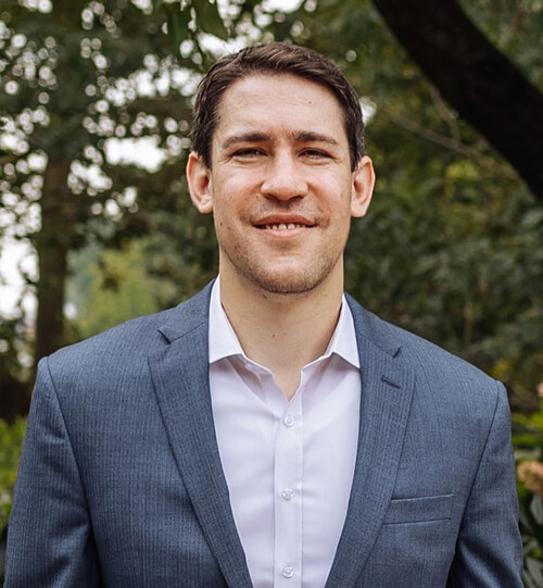 Headshot: Man in suit, smiling outdoors.