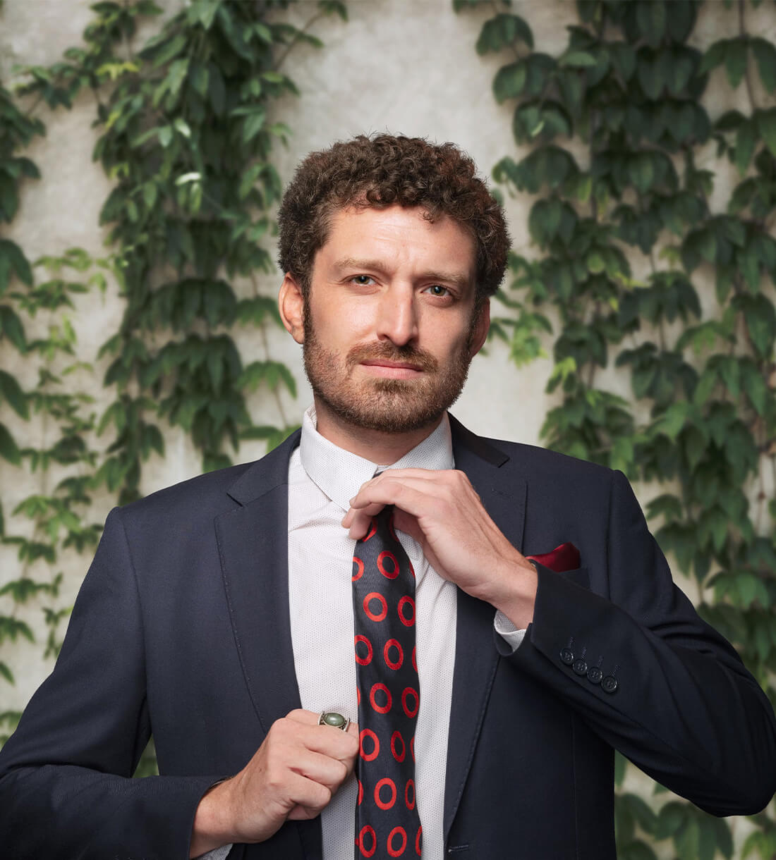 Man adjusting tie in front of ivy.